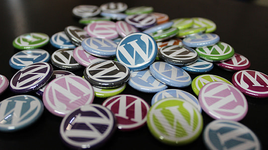 Badges colorés représentant le logo WordPress dispersés sur une surface sombre.