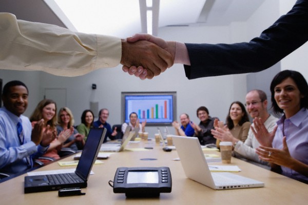 Poignée de main entre deux personnes dans une salle de réunion, symbolisant un accord réussi après une présentation de pitch deck devant des investisseurs attentifs.