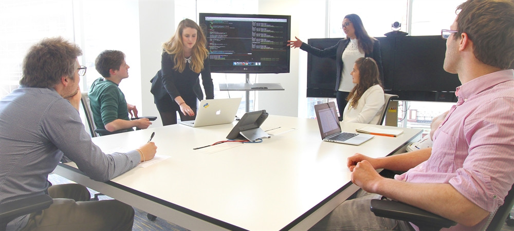 Une réunion professionnelle où des collaborateurs analysent des données sur un écran pour préparer un benchmark et optimiser leurs performances.